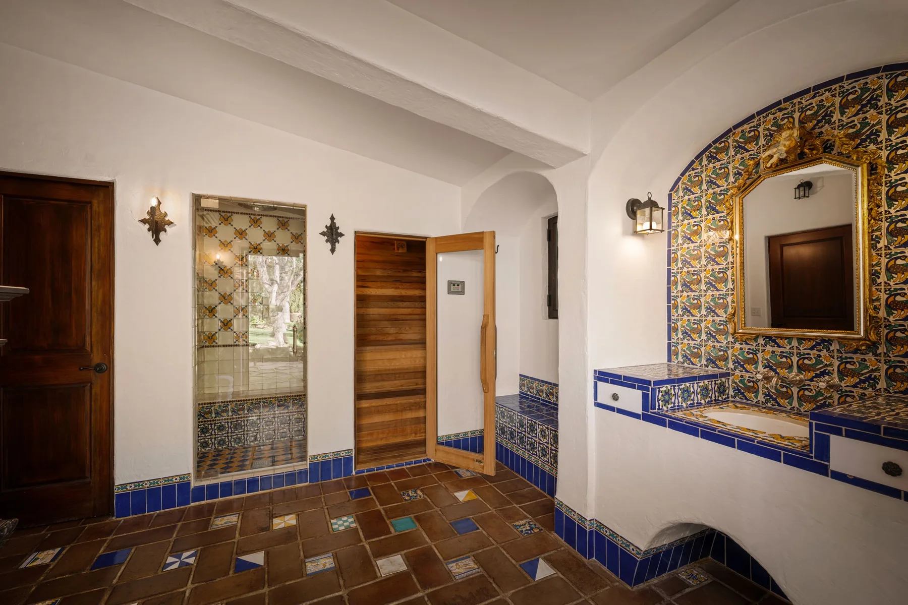 Un baño con azulejos, un espejo decorativo grande y una puerta de madera abierta.