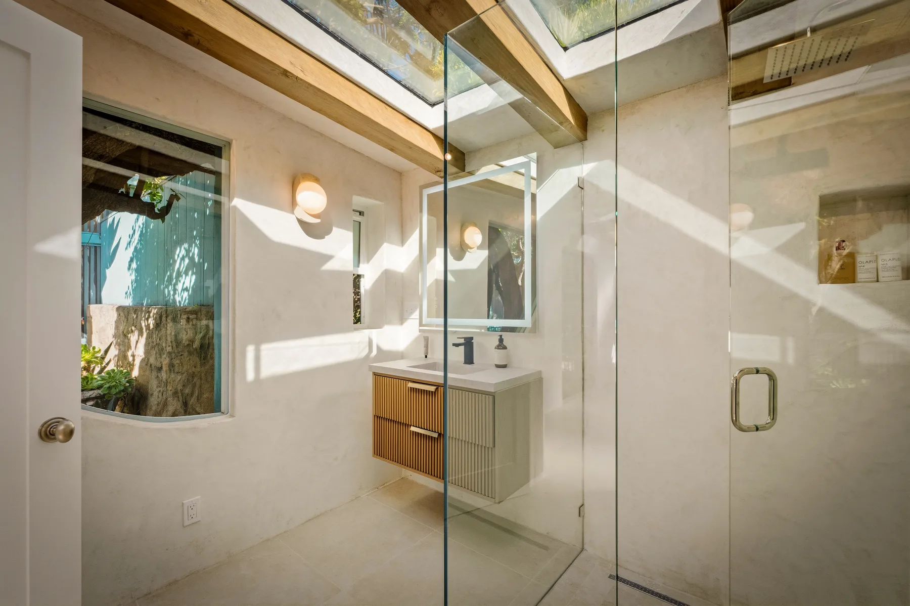 Un baño luminoso con una ducha de vidrio y un tocador debajo de un espejo.