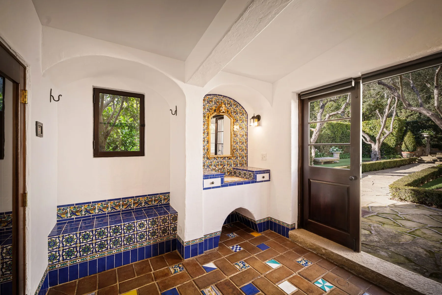 Un recibidor con azulejos, un espejo decorativo y una puerta abierta al jardín.