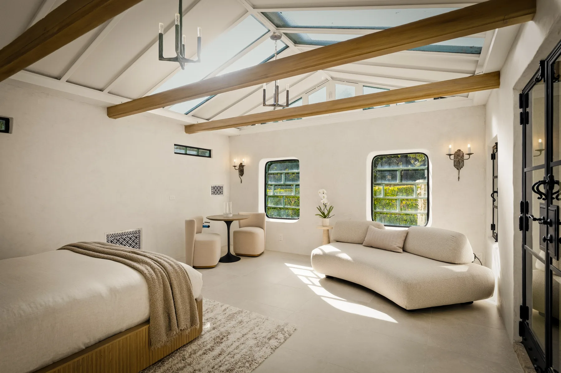 Un dormitorio luminoso con una cama, un sofá bajo y tragaluces.
