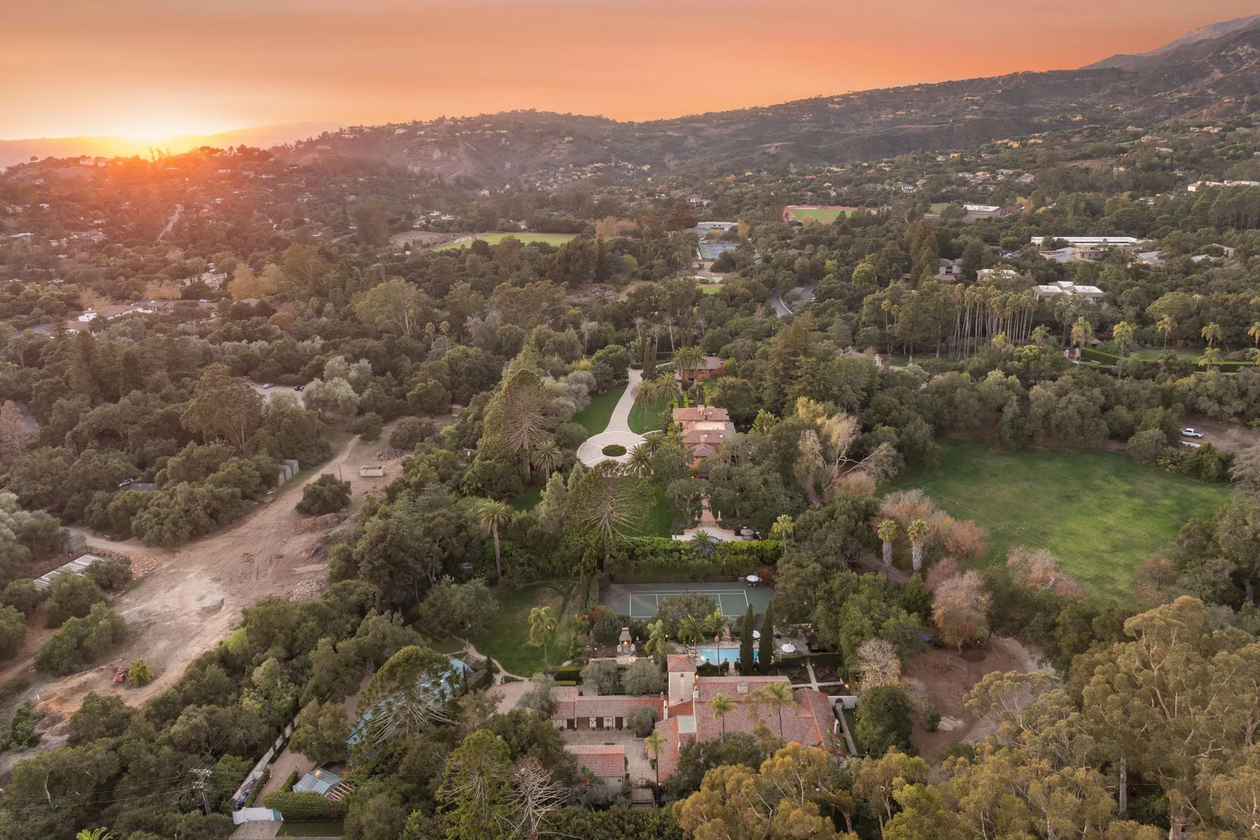 Vista aérea de un paisaje arbolado con casas y colinas al atardecer.