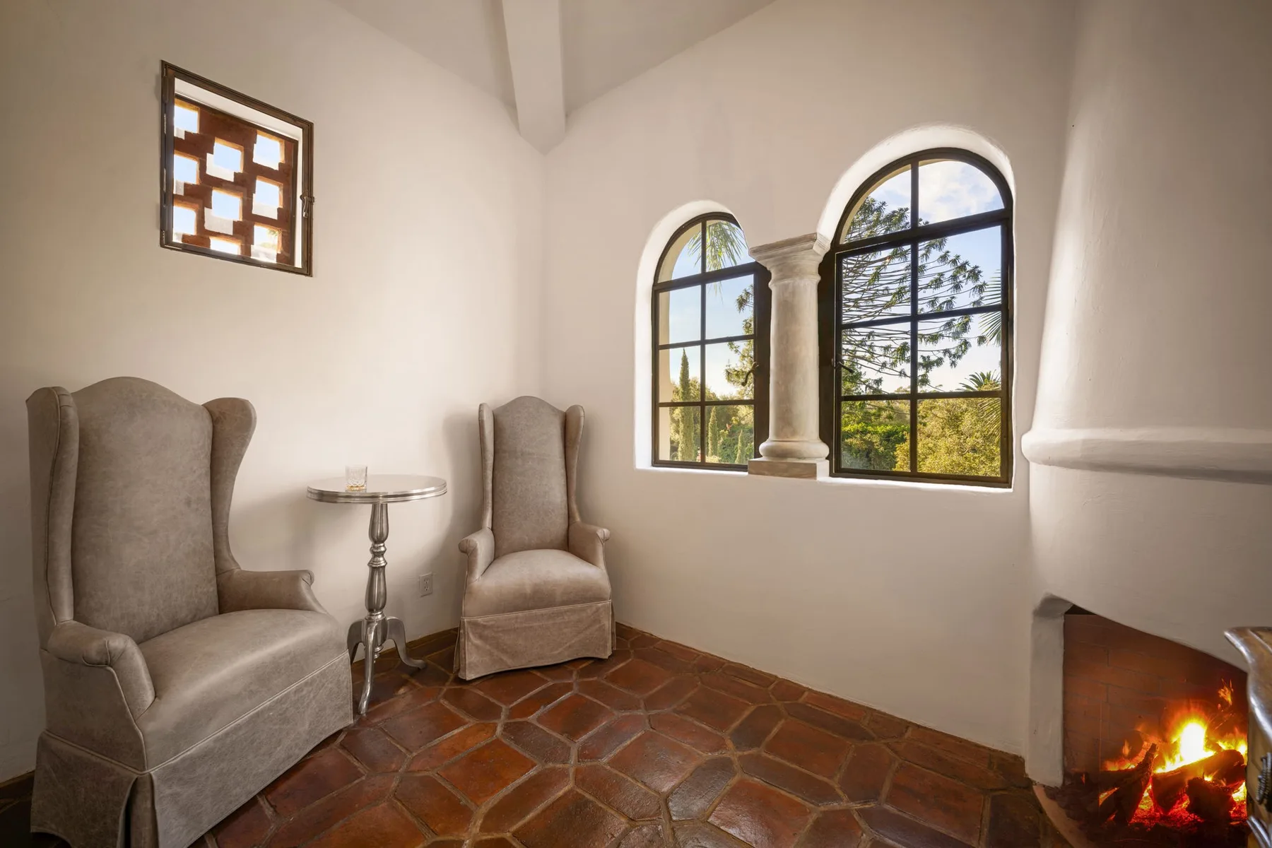 Una zona de estar con asientos tapizados, ventanas arqueadas y una chimenea encendida.