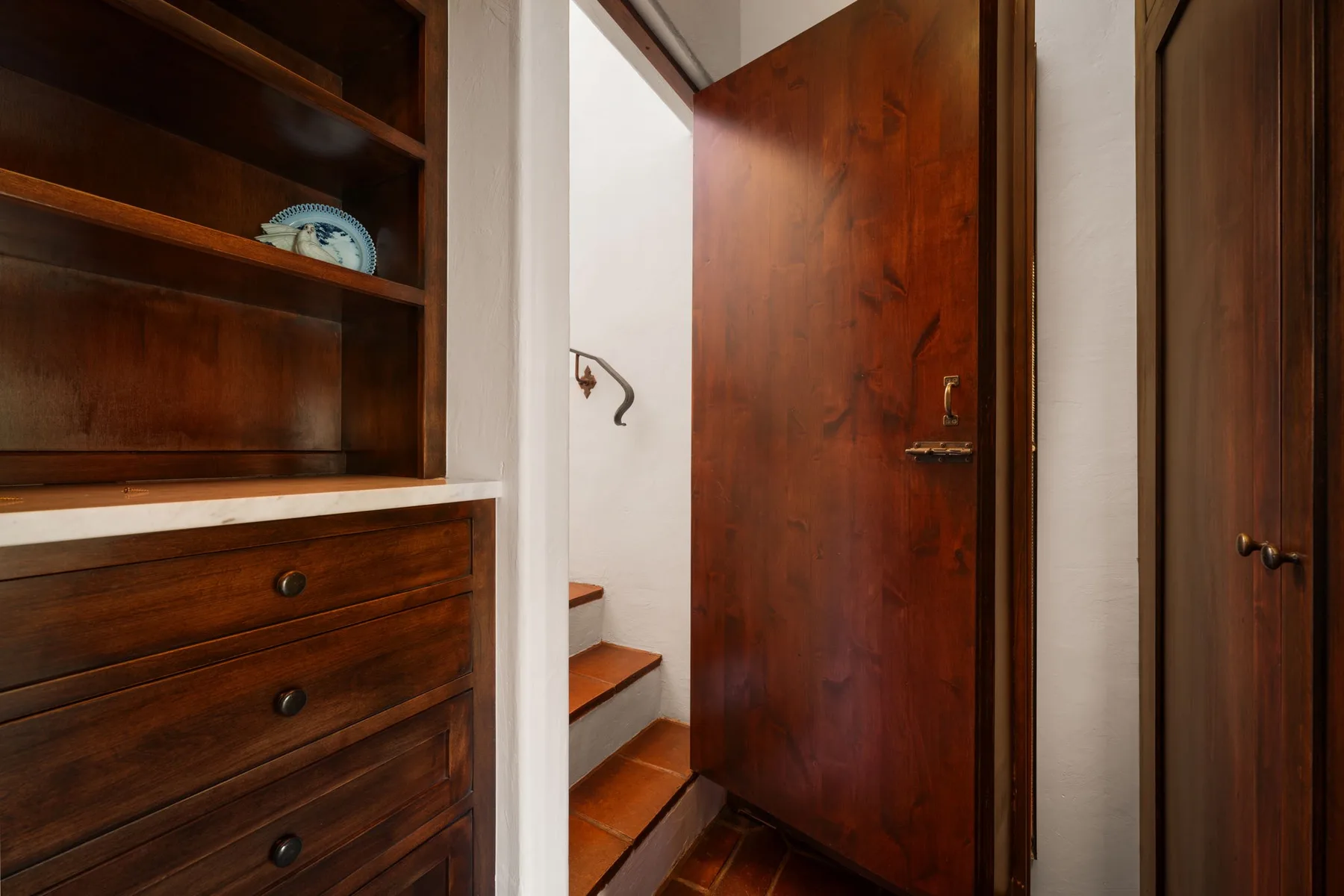 Una entrada de madera con estantes empotrados y una escalera junto a una puerta abierta.