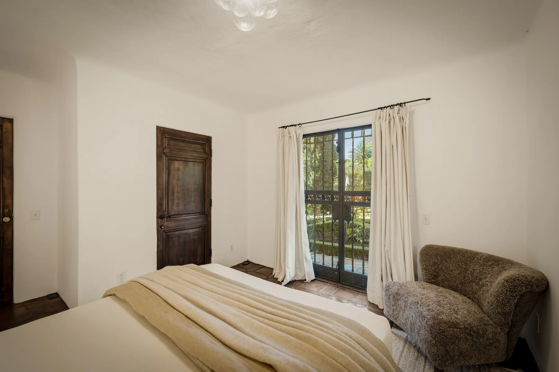 Dormitorio con una cama, una puerta de madera oscura y puertas de vidrio que dan a un balcón.