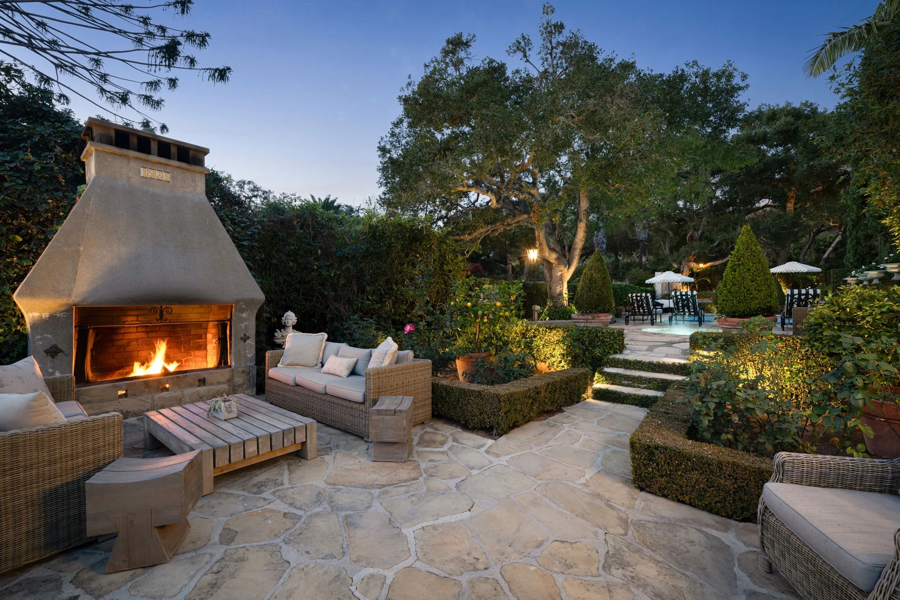 Un patio al aire libre con chimenea de piedra, asientos y jardín.