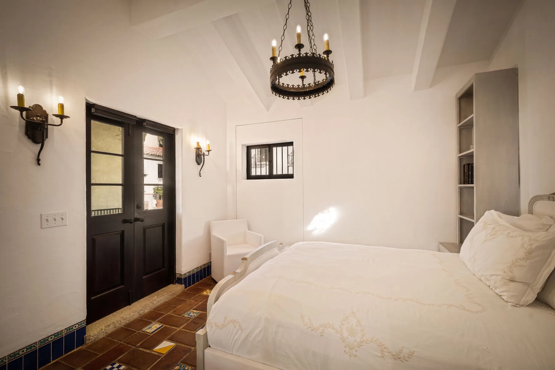 Un dormitorio luminoso con una cama grande, puertas oscuras y una lámpara colgante.