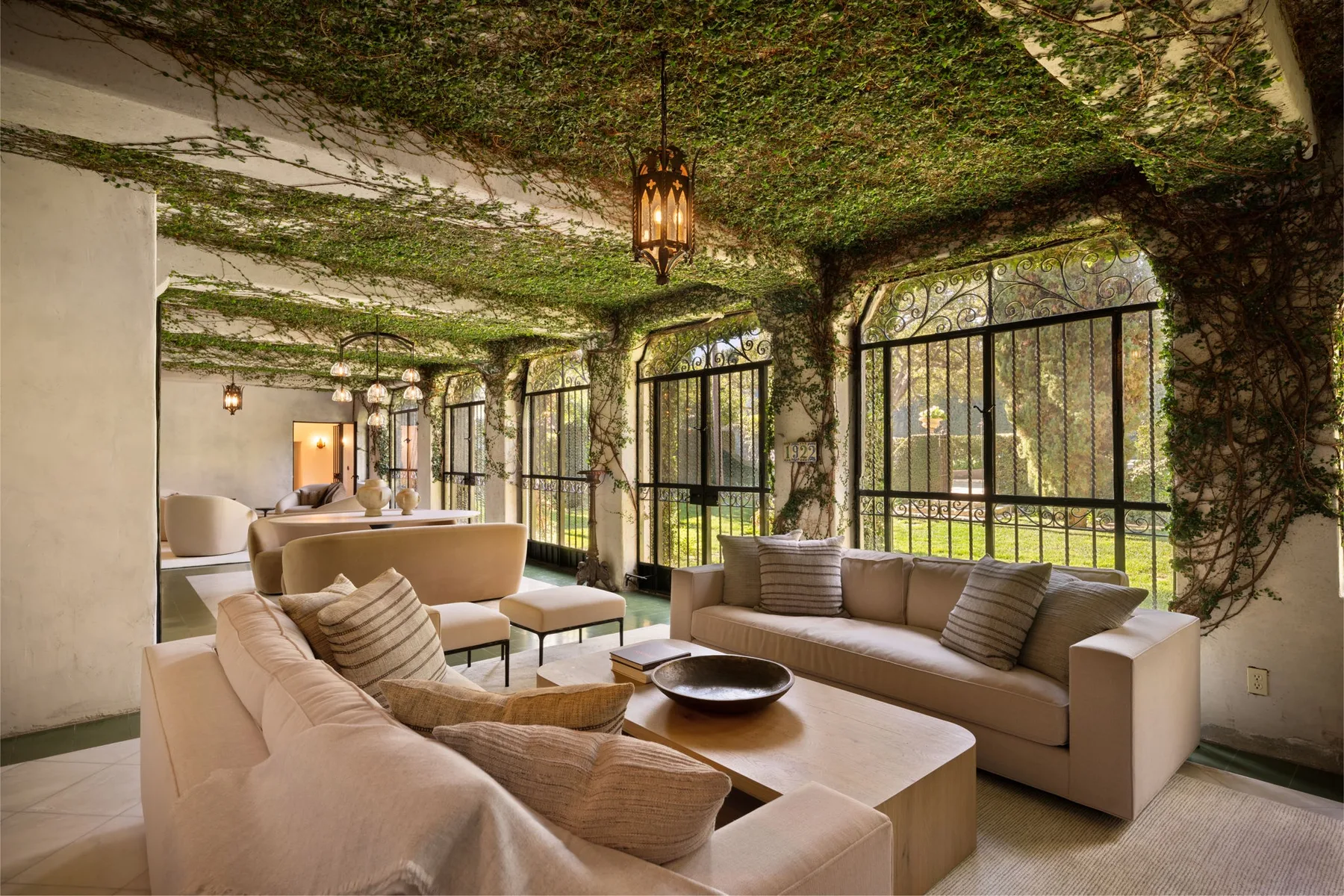 Una sala con asientos acolchados bajo un techo frondoso junto a grandes ventanas.