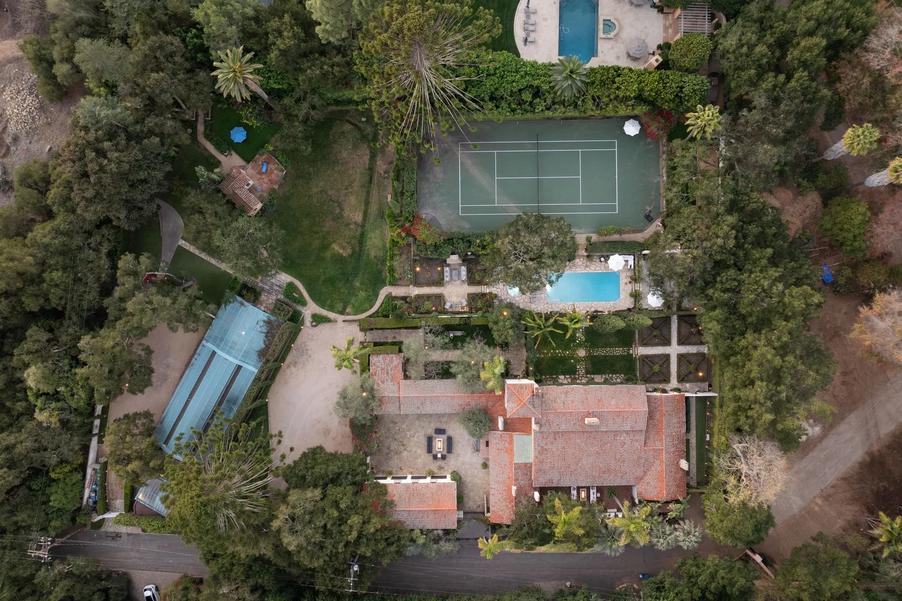 Vista aérea de una propiedad ajardinada con una cancha de tenis y una piscina.