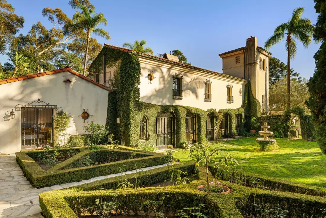 Un gran edificio de estuco se alza detrás de jardines formales y una fuente.