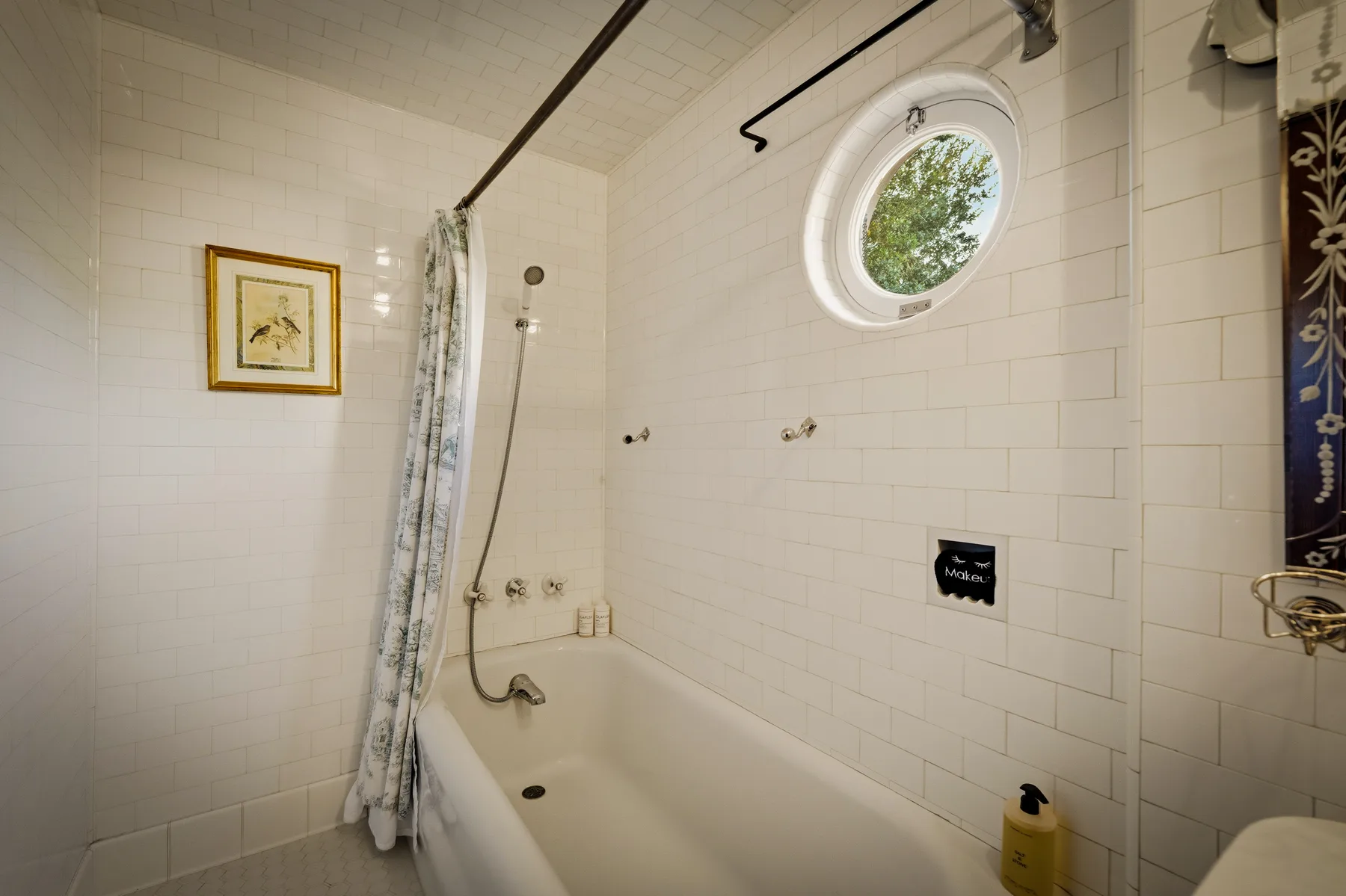 Un baño alicatado con bañera, cortina de ducha y ventana redonda.