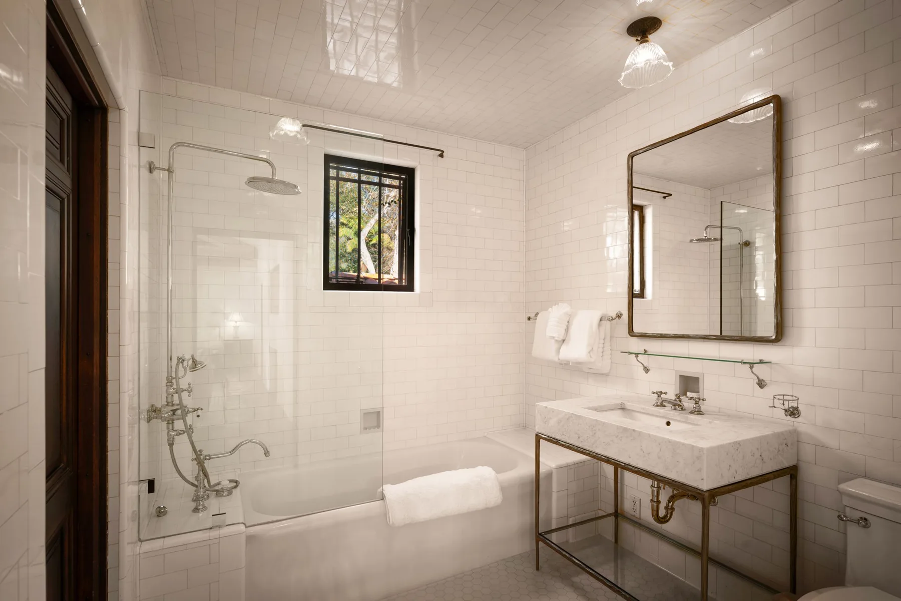 Un baño luminoso con azulejos, una ducha de vidrio y un lavabo bajo un espejo grande.