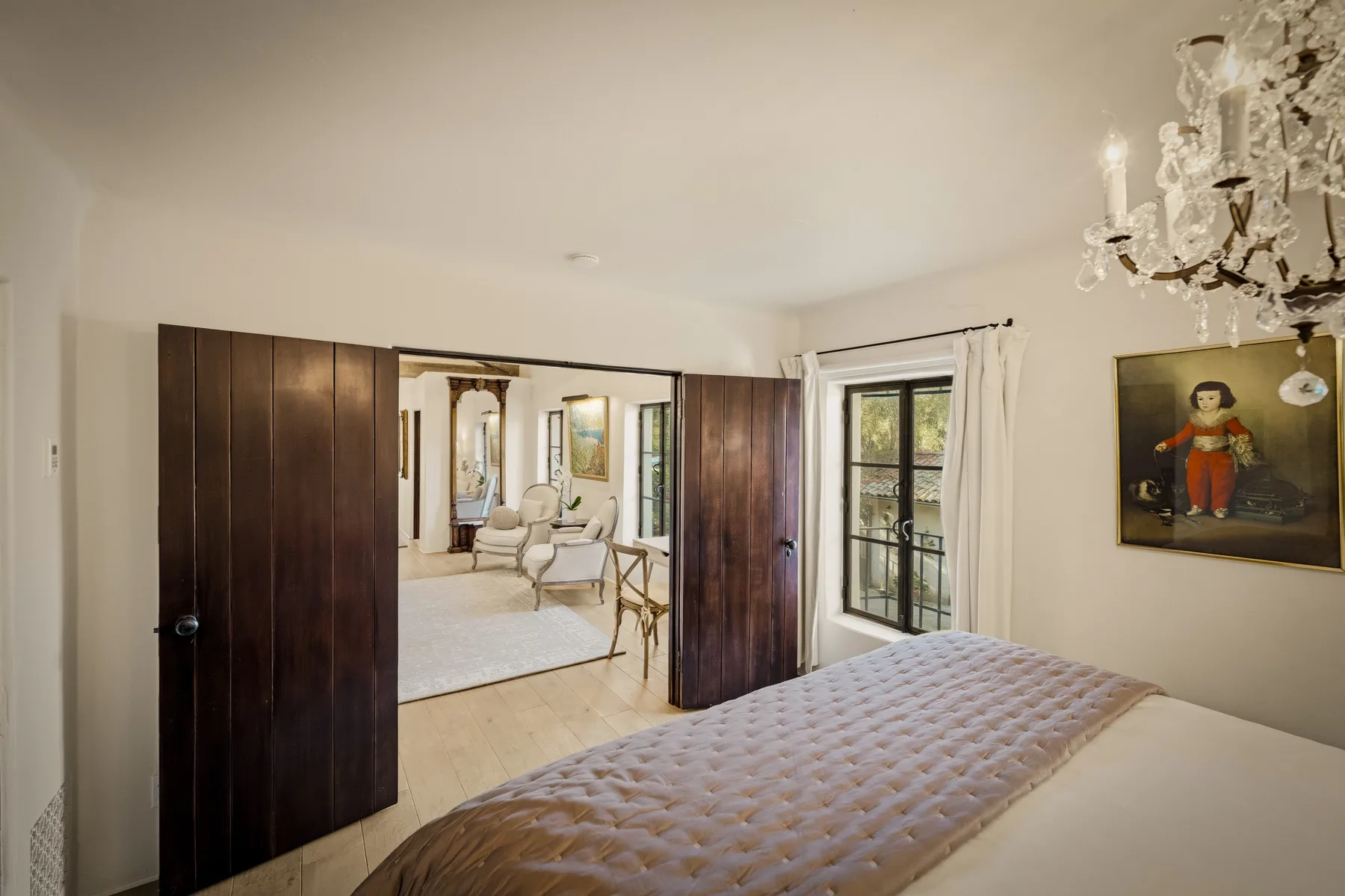 Un dormitorio con una cama, puertas de madera oscura abiertas y una puerta de vidrio al balcón.