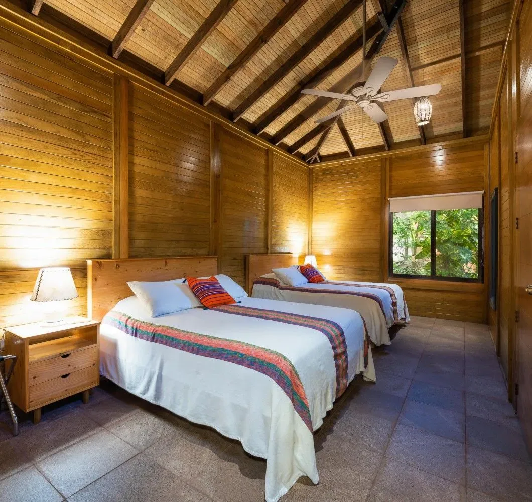 Dormitorio de madera con dos camas individuales y un ventilador de techo.