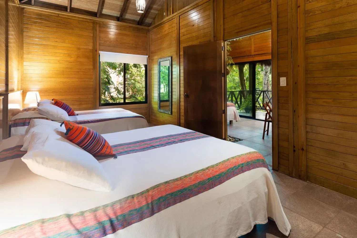 Dormitorio con una cama blanca y puertas abiertas hacia una frondosa vegetación.
