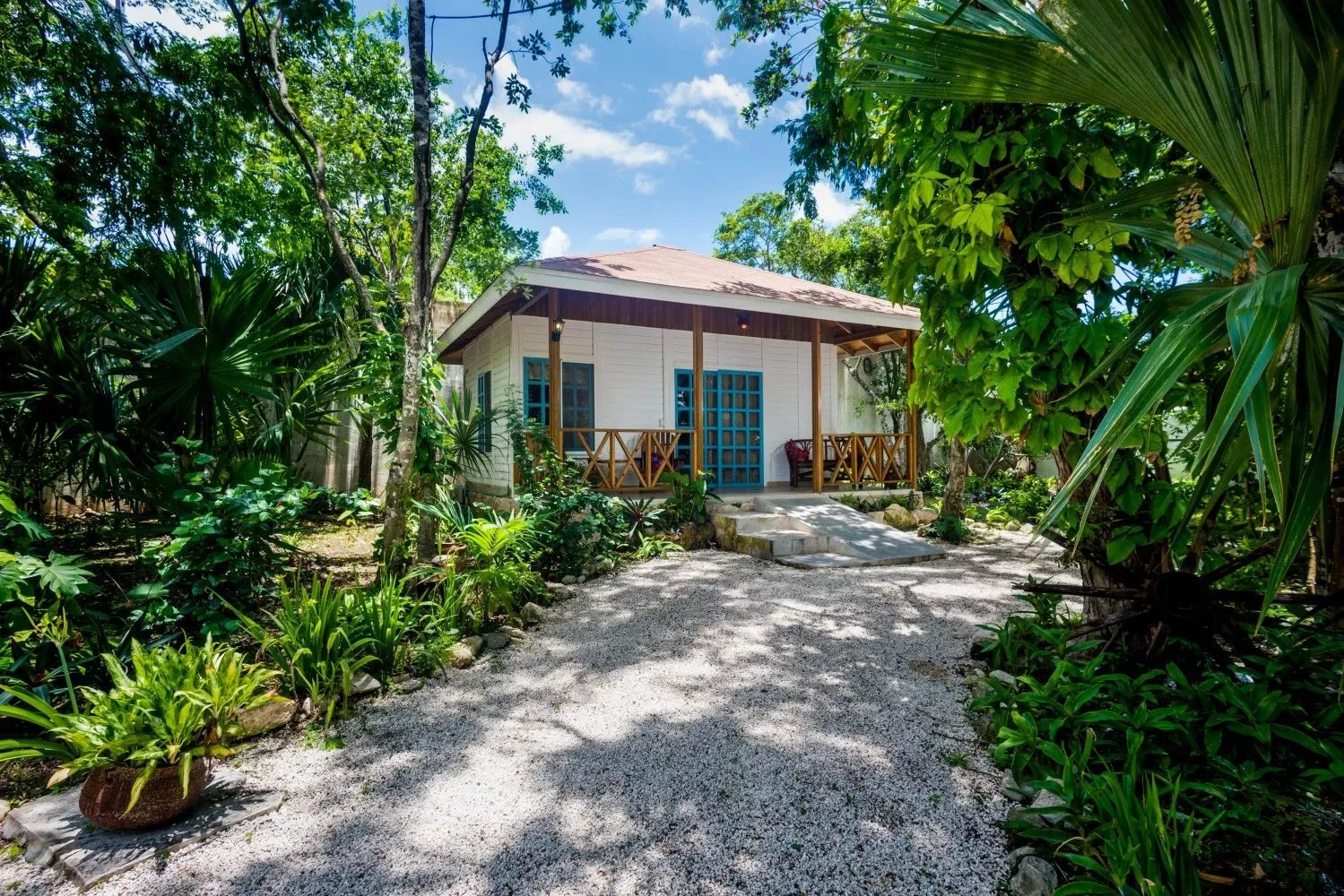 Pequeño bungaló junto a un sendero de grava entre vegetación tropical.