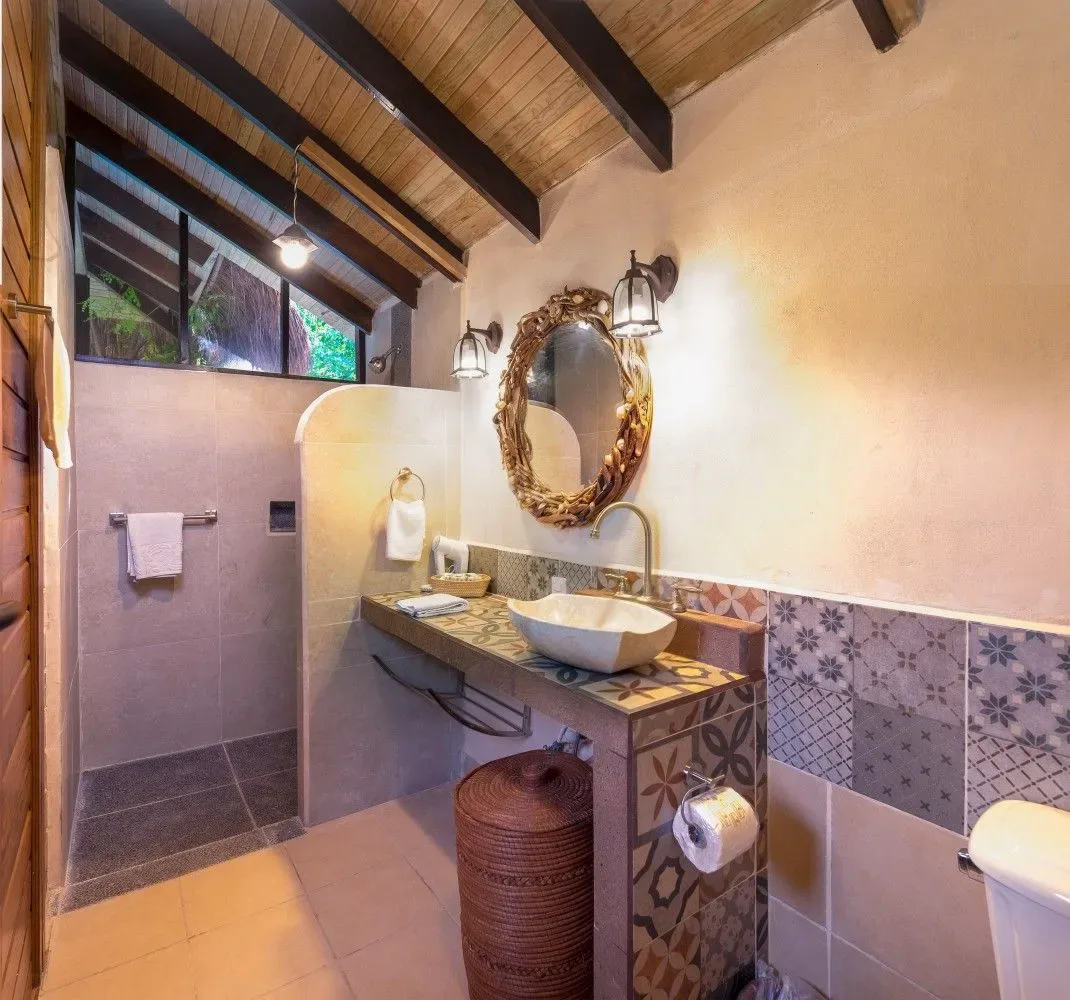 Baño de piedra y madera con lavabo sobre encimera y ducha abierta.