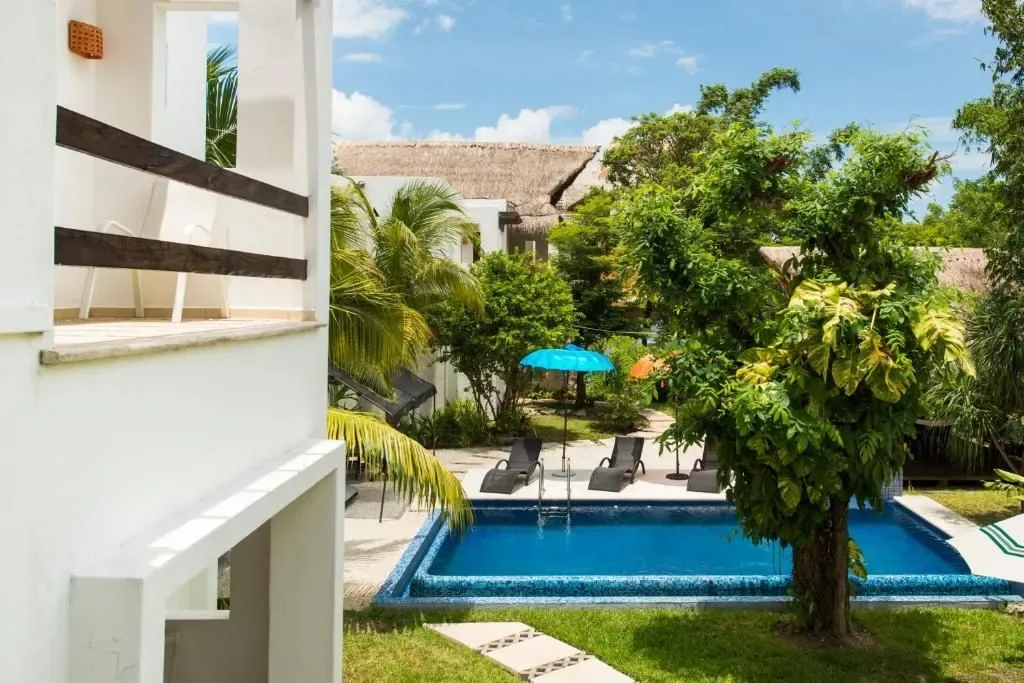 Patio de hotel con piscina, palmeras, tumbonas y una sombrilla turquesa.