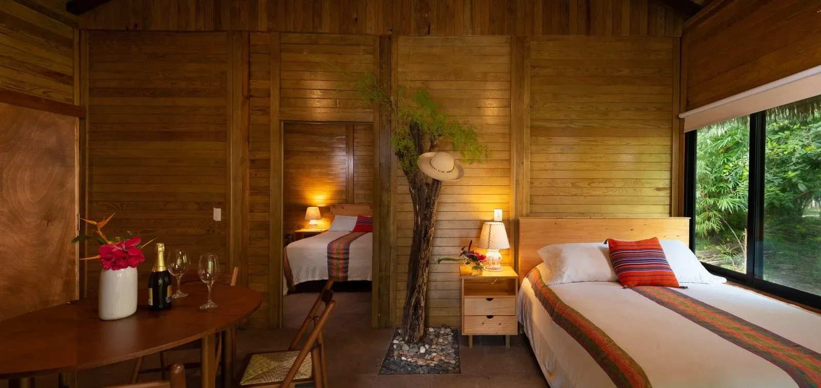 Dormitorio de bambú con dos camas y vistas a la vegetación.