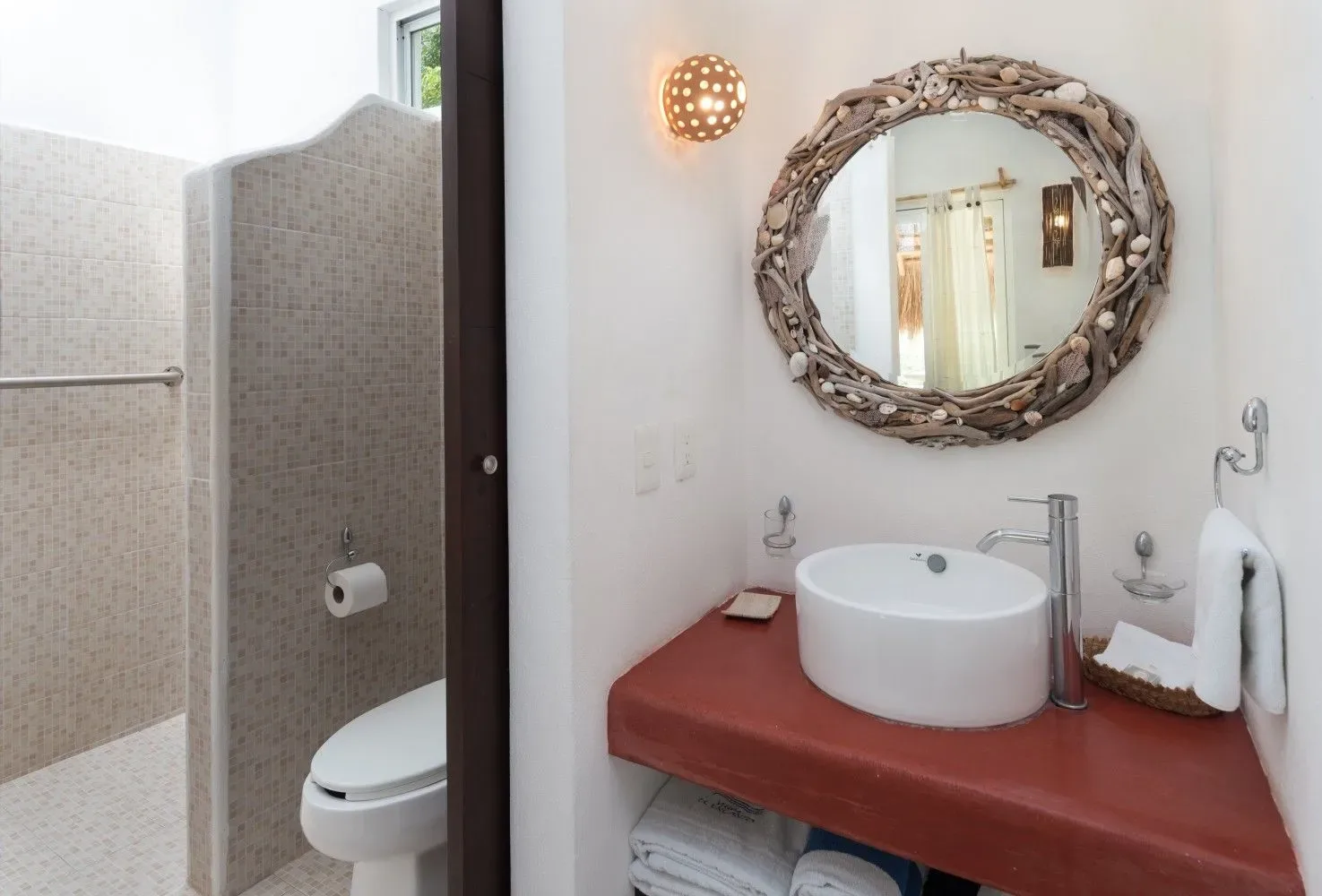 Baño con inodoro, lavabo sobre encimera y espejo redondo.