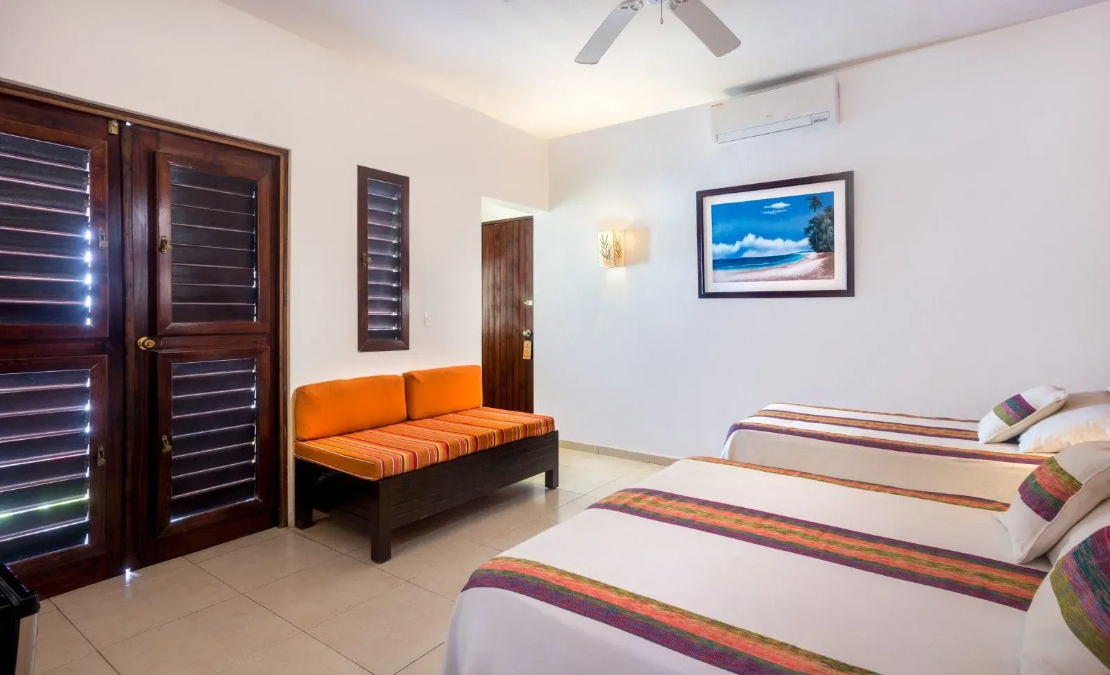 Dormitorio con camas individuales, un banco naranja y contraventanas.
