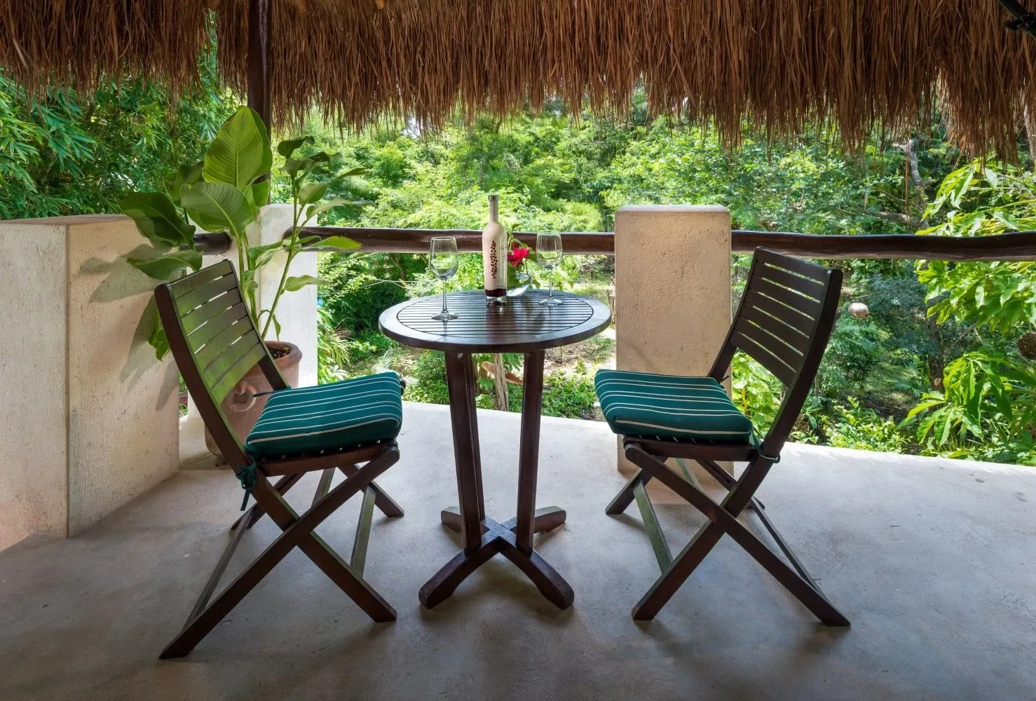 Patio con techo de paja, sillas y una mesa con vistas a la vegetación.