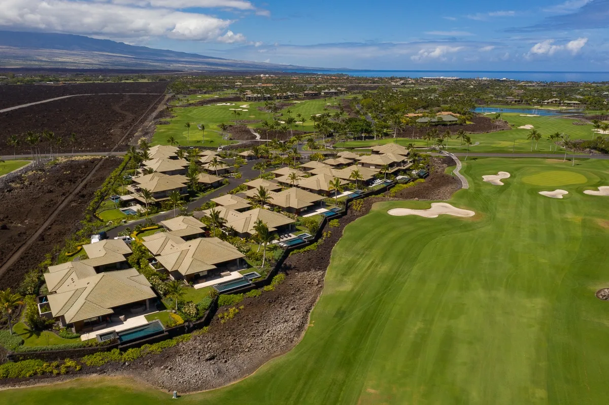 Aerial view of a golf course beside a cluster of buildings and landscaped grounds.