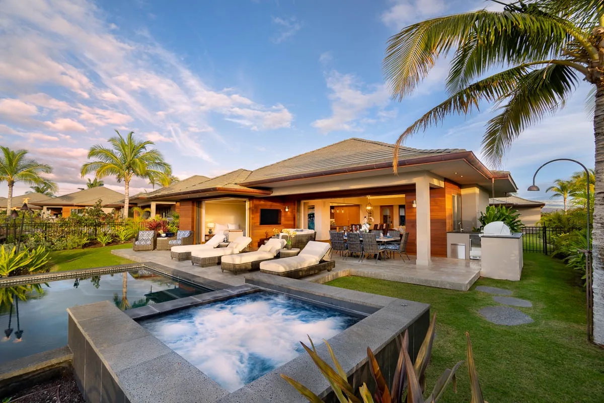 A patio beside a pool and bubbling spa, with outdoor seating under a covered roof.