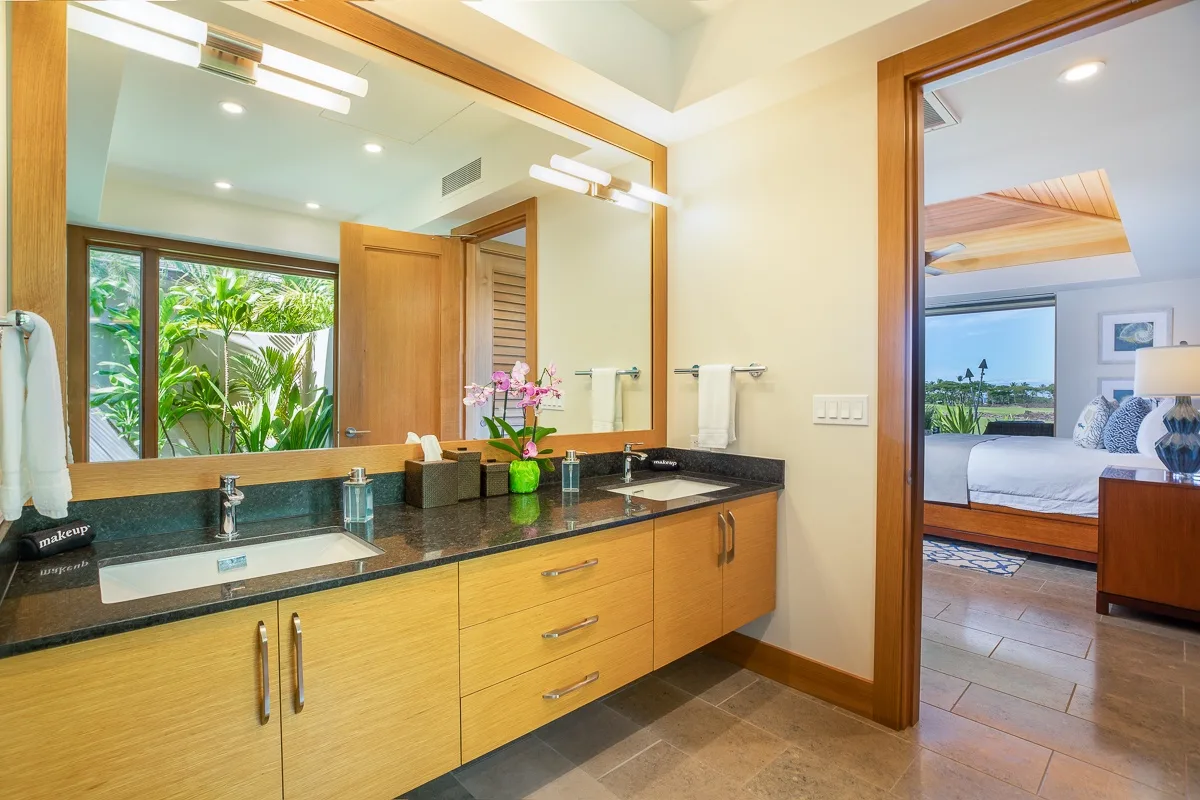 A bathroom vanity with a wide mirror and a doorway into a bedroom.