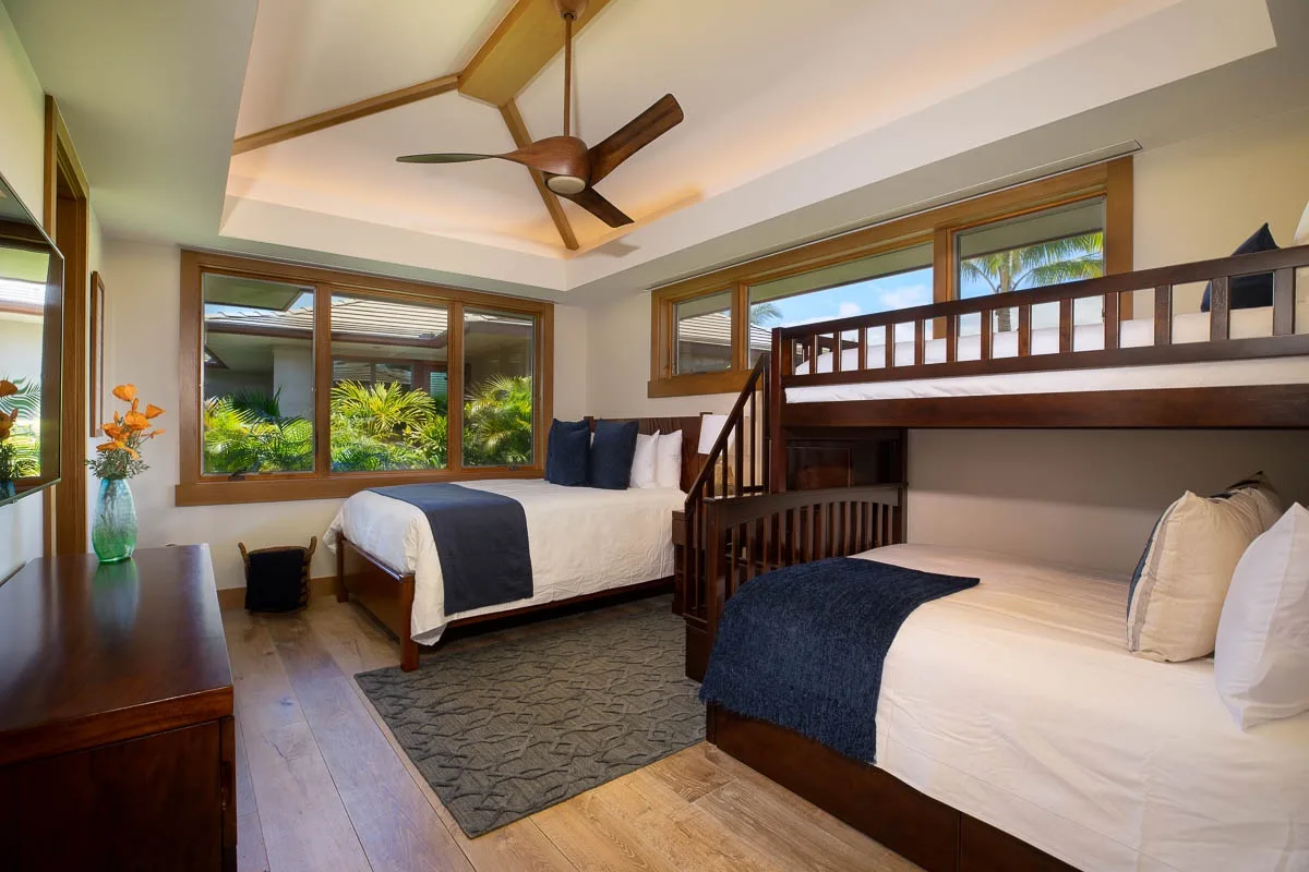 A bedroom with two beds, dark wooden frames, and large windows overlooking greenery.