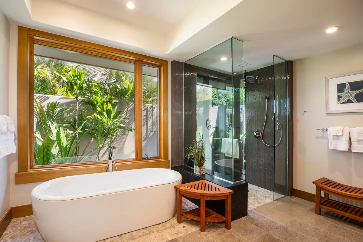 A bathroom with a bathtub beside a glass shower and a large window.