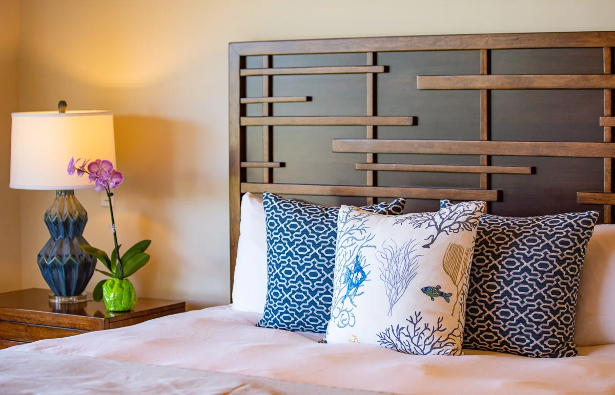A bedroom with a bed, patterned pillows, and a bedside lamp.