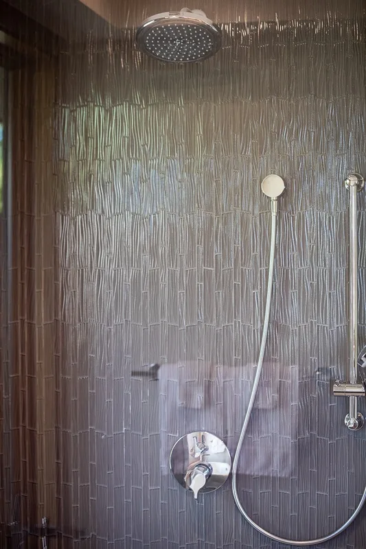 A tiled shower with a round overhead showerhead and handheld shower.