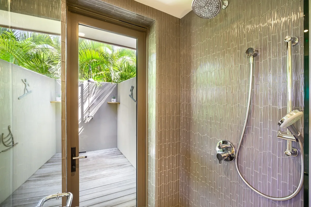 A shower area opens onto a small outdoor patio with tropical greenery.