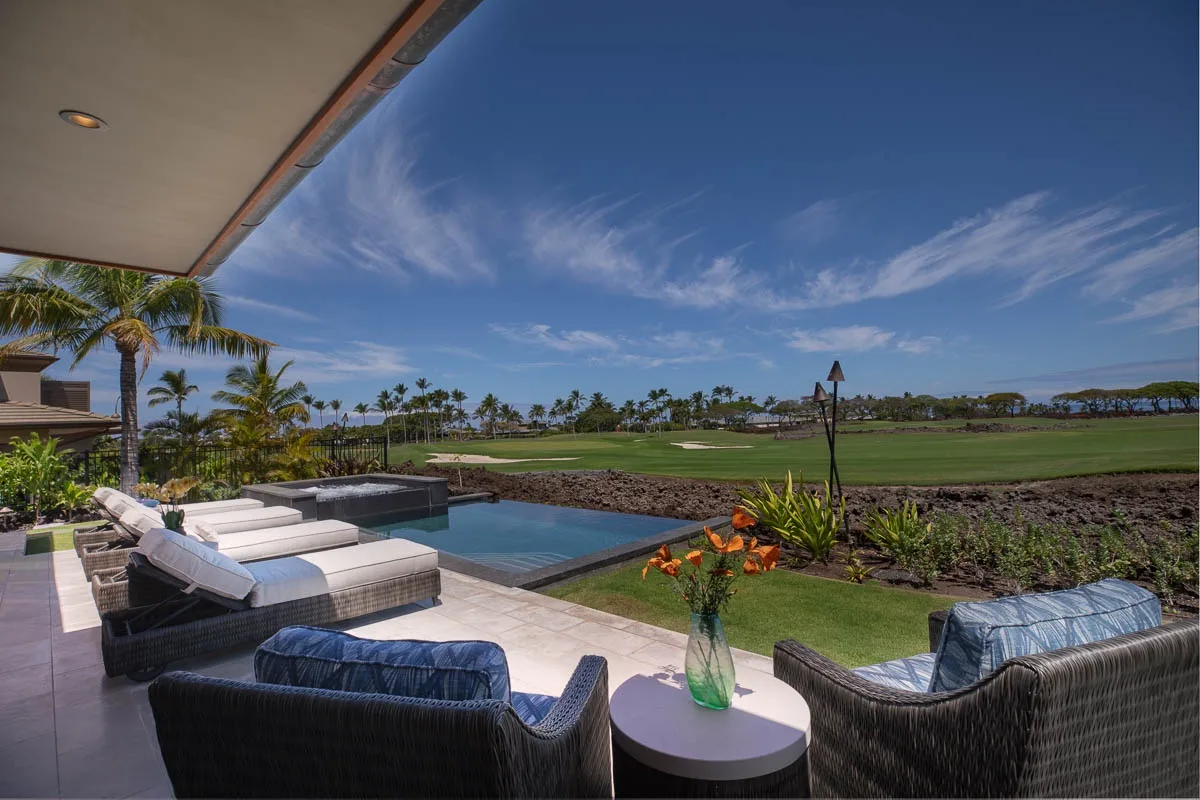 An outdoor patio with cushioned seating overlooks a swimming pool and golf course.