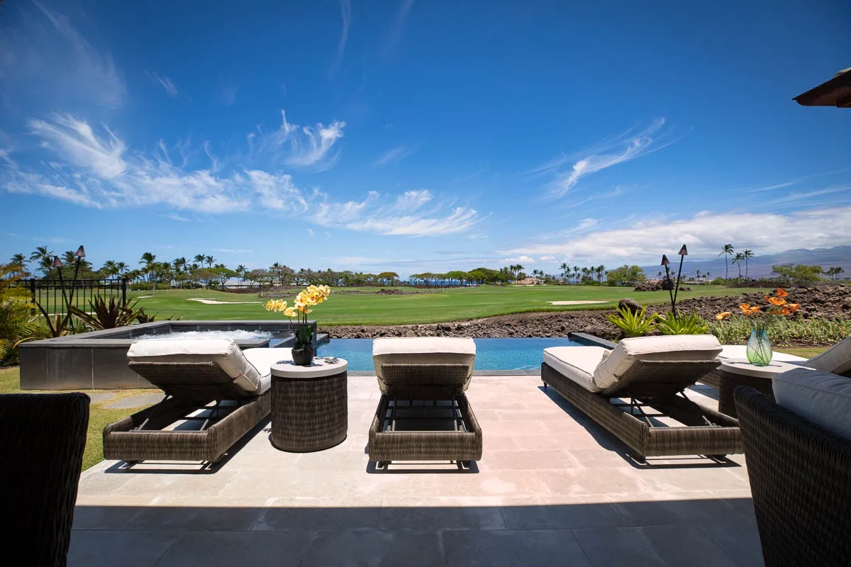 A patio with lounge seating overlooks a pool and green landscape.
