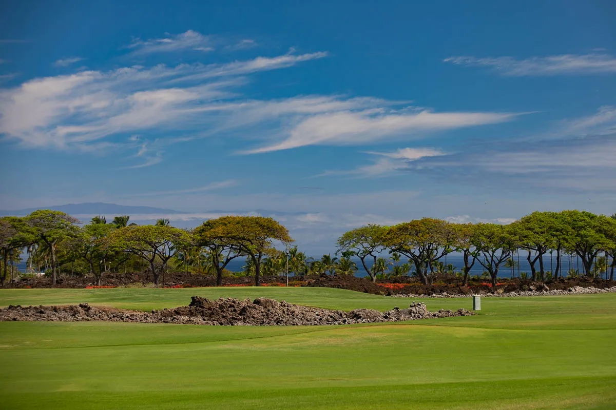 A broad green golf course stretches beneath a blue, cloud-streaked sky.