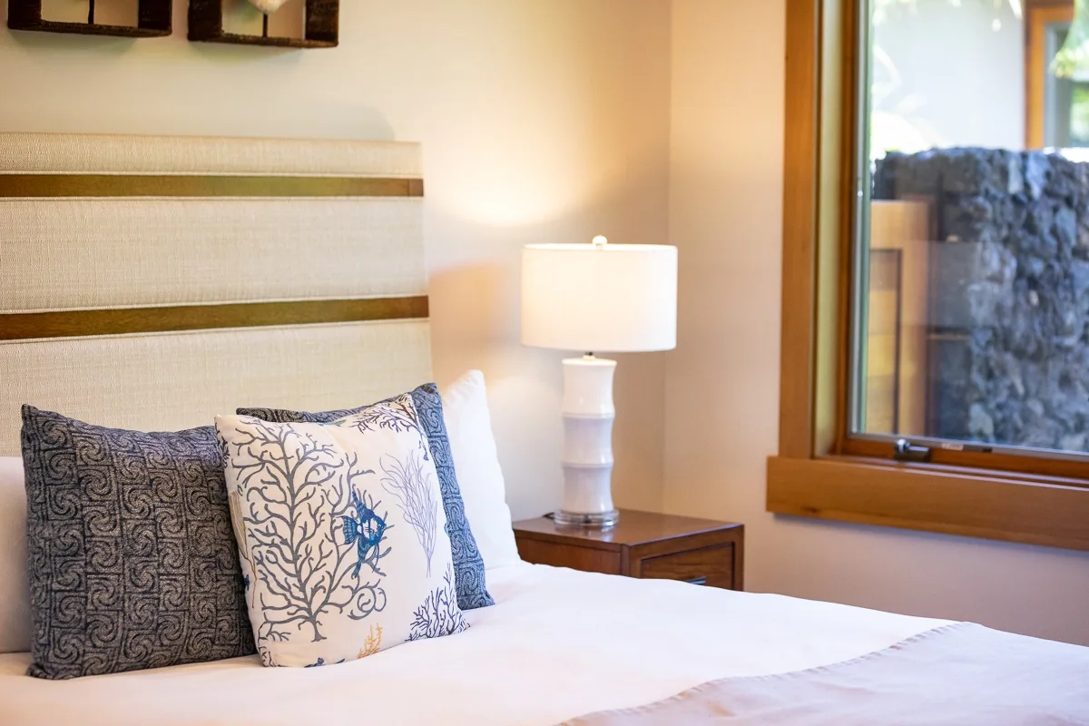 A bedroom with a neatly made bed, patterned pillows, and a bedside lamp.
