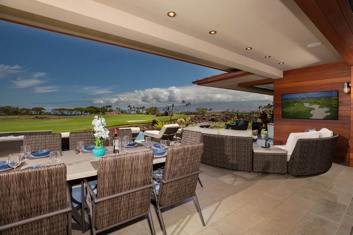 A covered outdoor dining area with a table and seating overlooks a green landscape.