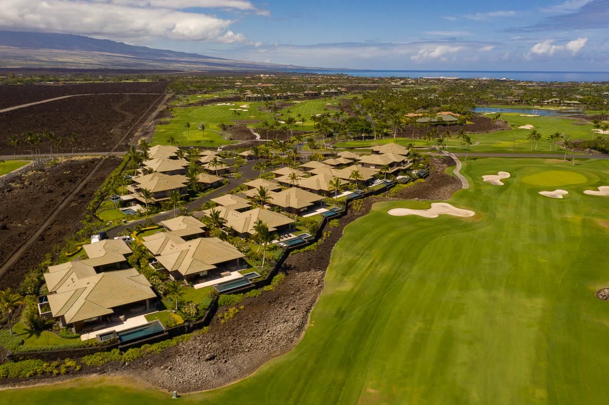 An aerial view shows buildings beside a golf course with green fairways and sand bunkers.