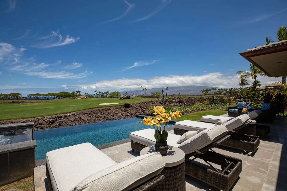 An outdoor pool beside cushioned seating overlooks a broad green landscape.