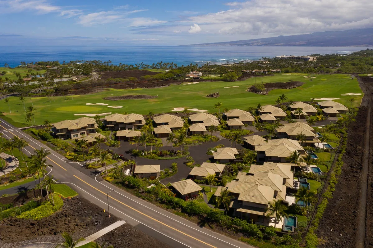 Aerial view of a coastal golf course beside a cluster of low-rise buildings.
