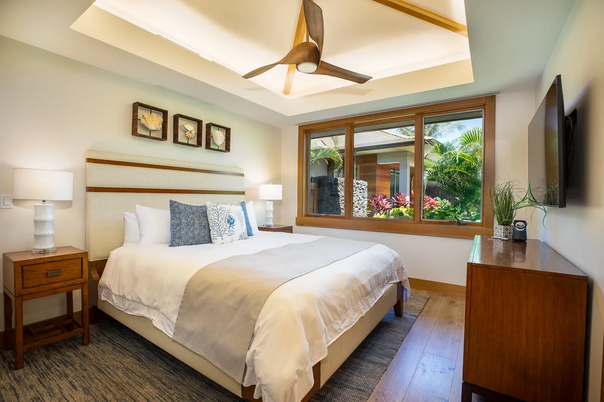 A bedroom with a neatly made bed, bedside tables, and a window overlooking greenery.