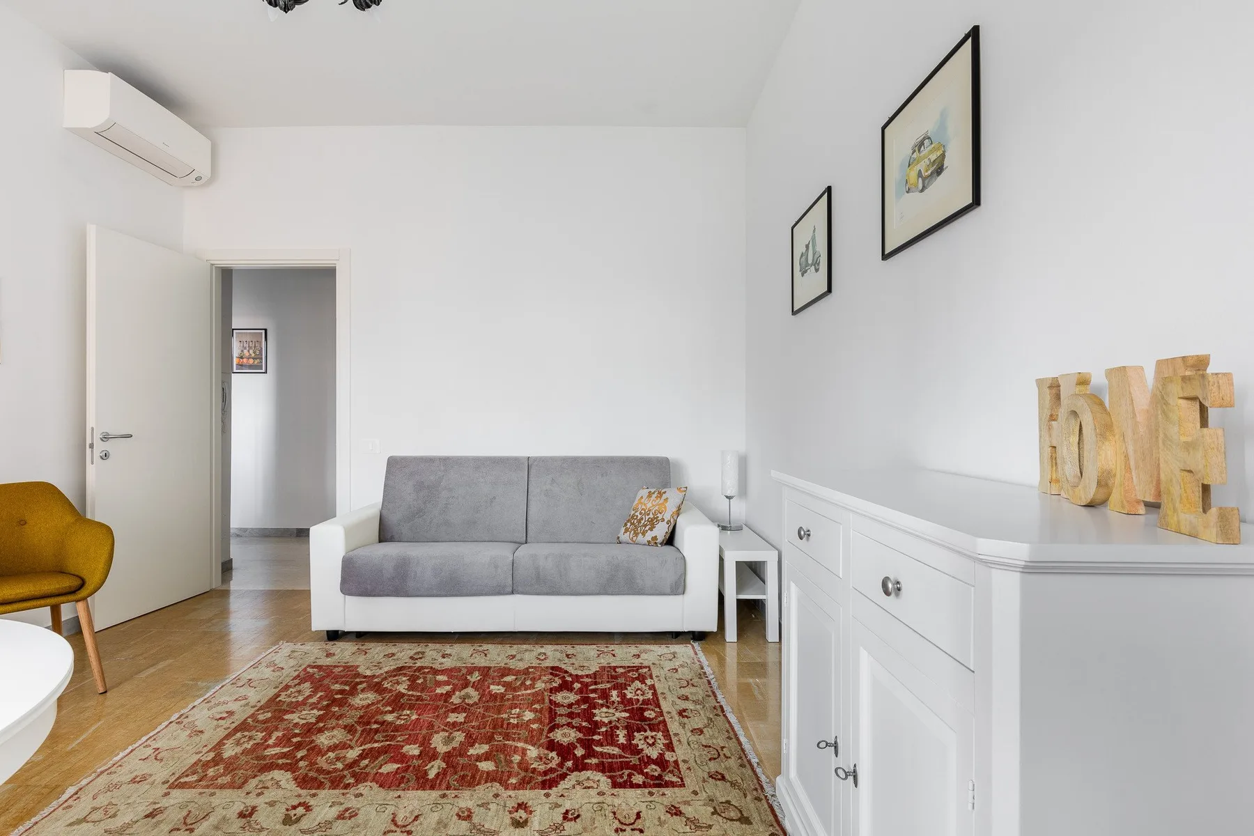 Una sala luminosa con un sofá gris y una alfombra estampada.