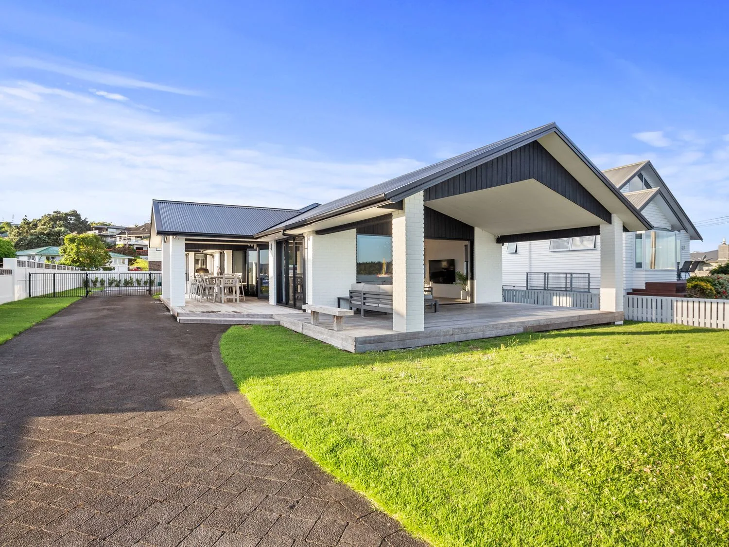 Una casa moderna tiene un patio cubierto junto a una entrada pavimentada y césped verde.