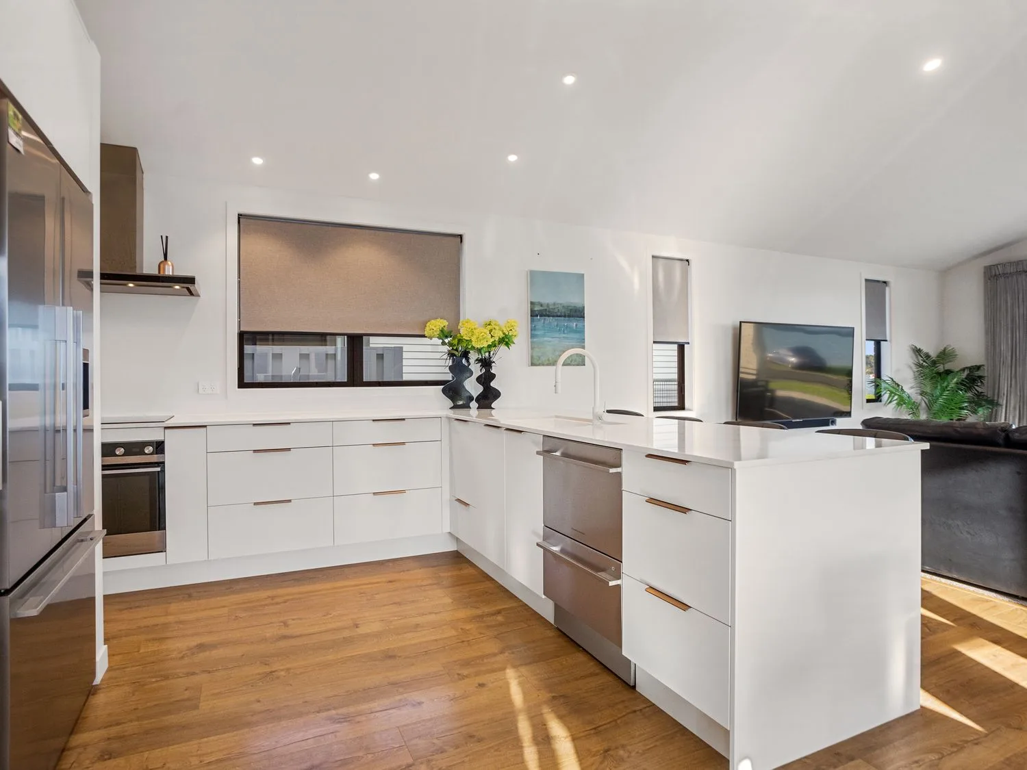 Una cocina moderna con armarios blancos, una isla grande, un fregadero y electrodomésticos de acero inoxidable en Waterfront Oasis Omokoroa Holiday Home, en Omokoroa