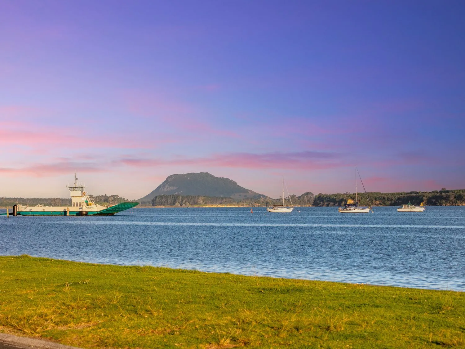 Un puerto costero con barcos en el agua y una montaña baja al otro lado de la bahía.