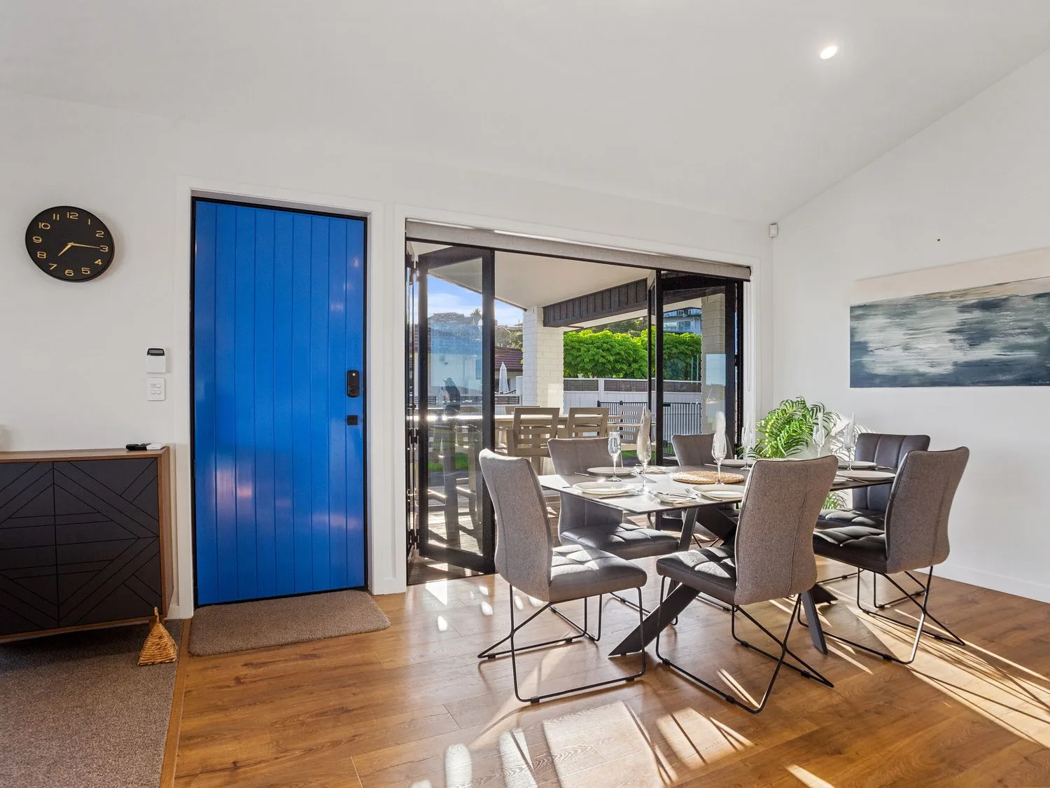 Un comedor con seis sillas alrededor de una mesa cerca de una puerta azul y puertas correderas de cristal en Waterfront Oasis - Omokoroa Holiday Home, en Omokoroa