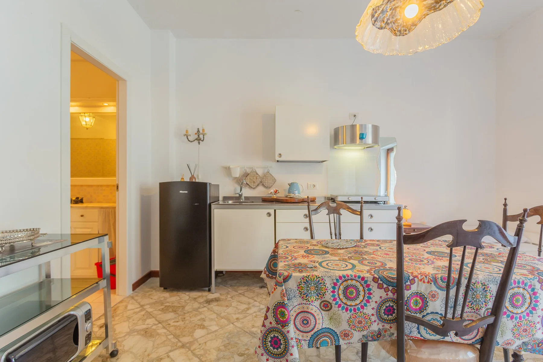 Comedor con un mantel estampado y una cocina compacta al fondo.