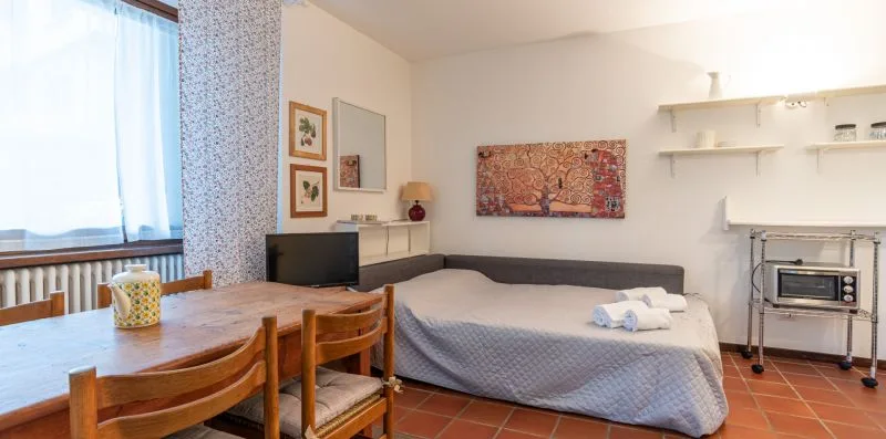 Un dormitorio con una cama, una mesa de madera y sillas junto a una ventana.