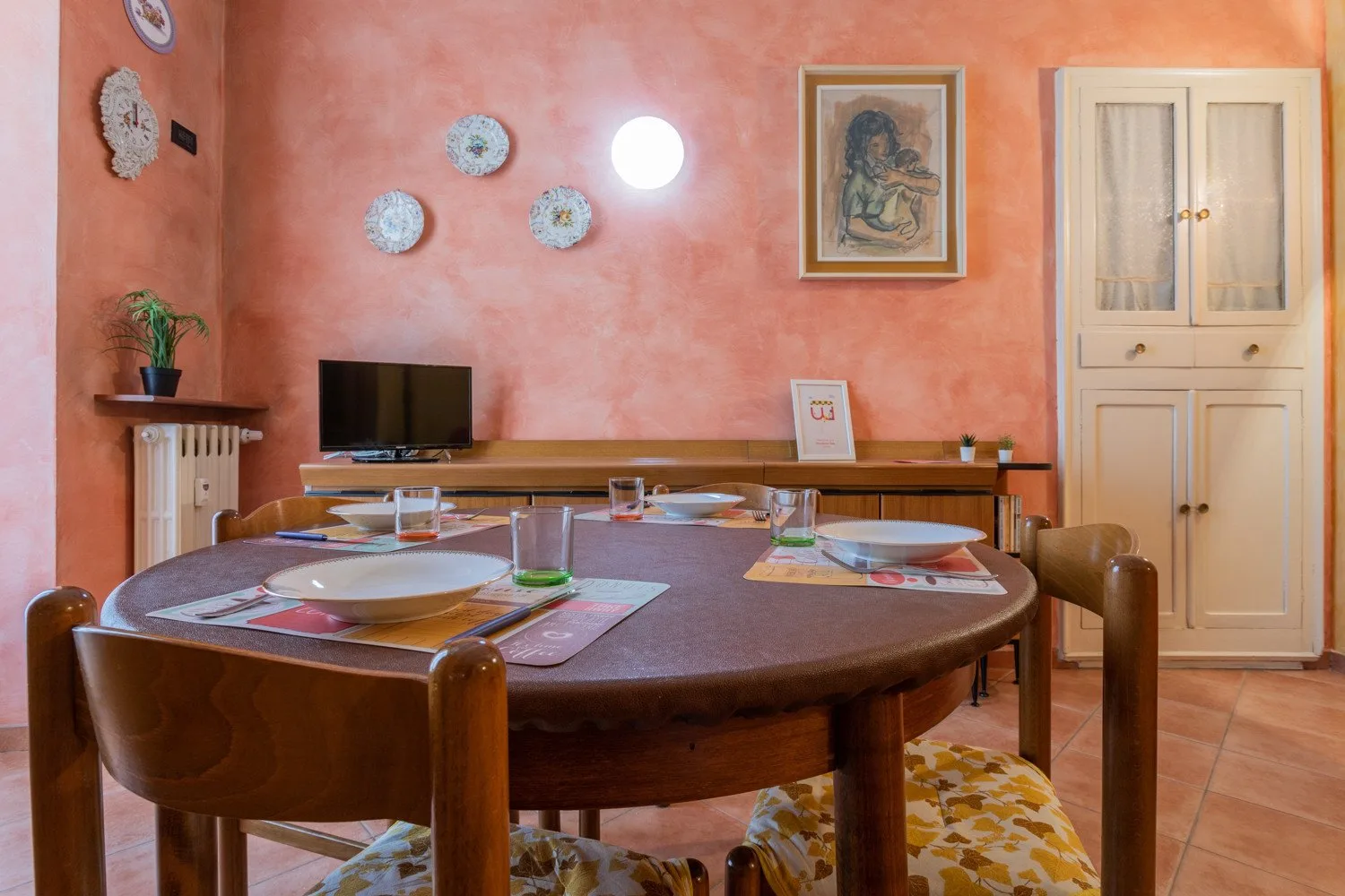 Un comedor con una mesa redonda puesta con platos y un televisor en la pared.